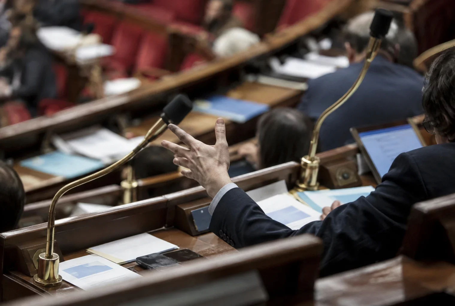 Pupitres équipés de microphones et documents de séance dans un hémicycle aux rangées incurvées de sièges.