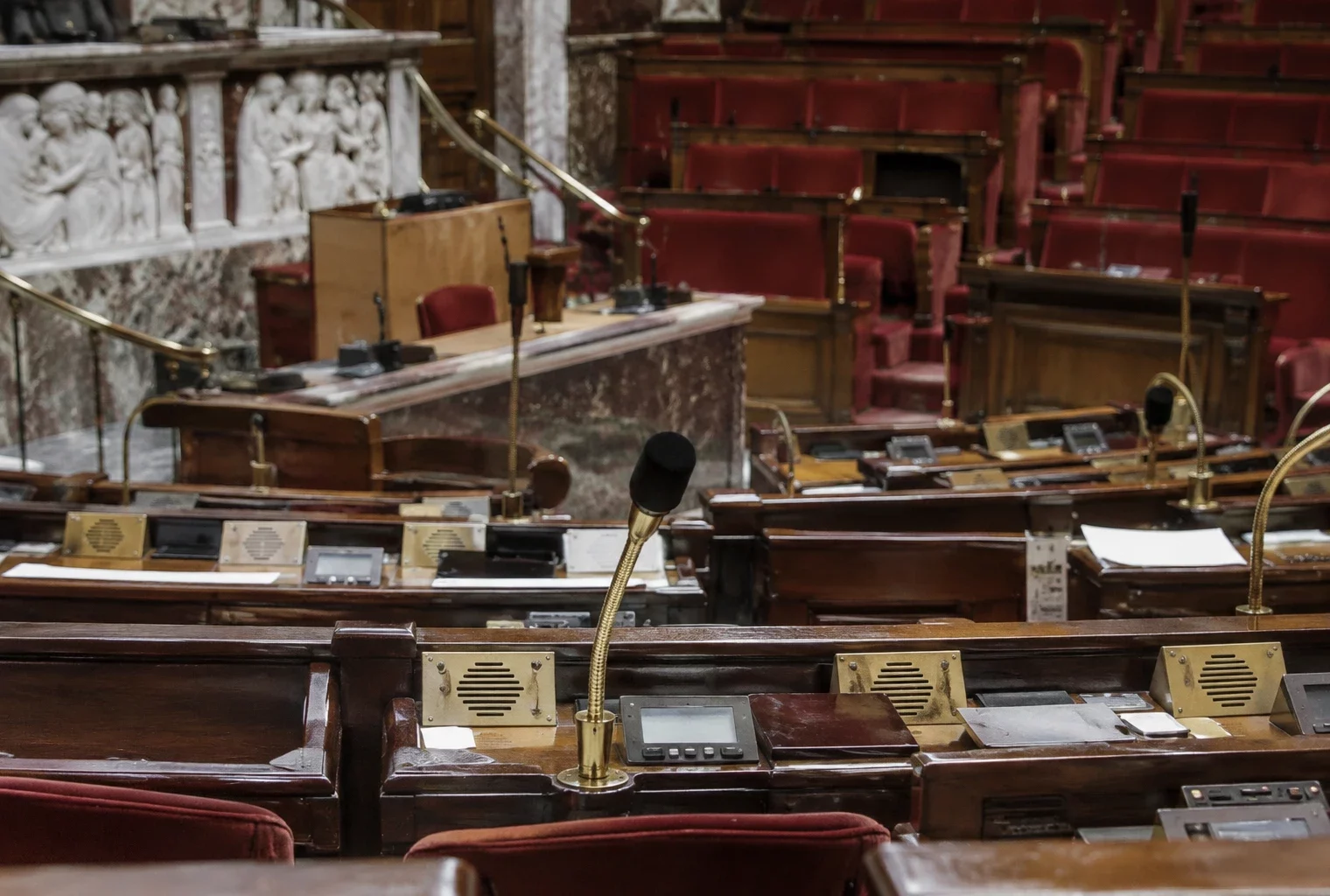Rangées de pupitres équipés de microphones dans un hémicycle parlementaire, avec les gradins de sièges en arrière-plan.