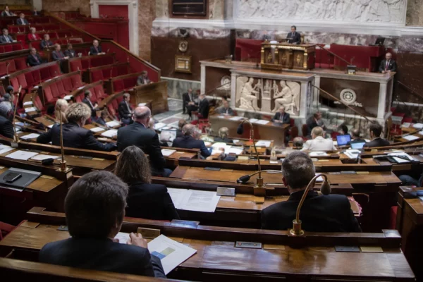 Pupitres équipés de microphones et de boîtiers de vote devant les rangées de sièges d’un hémicycle parlementaire.