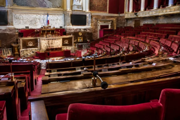 Pupitres équipés de microphones dans un hémicycle parlementaire, avec des rangées de sièges et une tribune au fond.