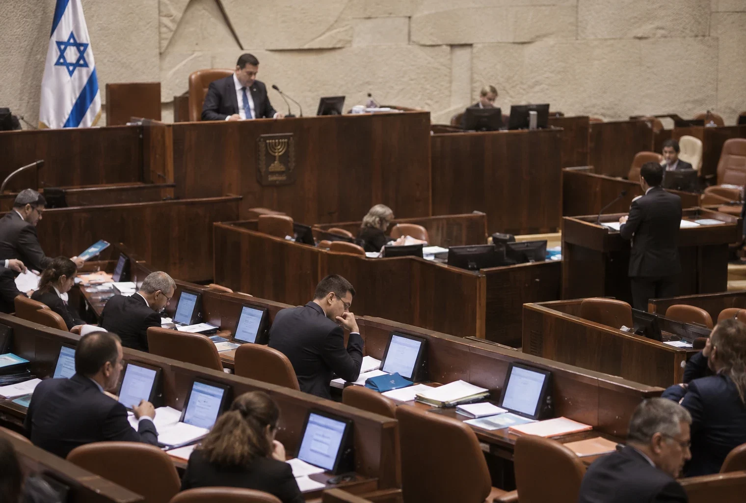 Rangées de sièges et de pupitres équipés de microphones dans un hémicycle parlementaire sans occupants.