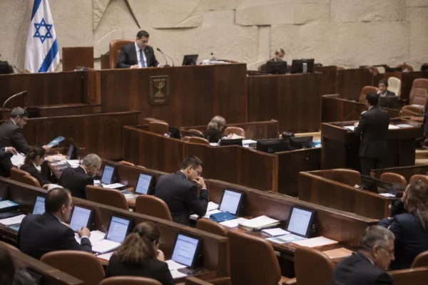 Rangées de sièges et de pupitres équipés de microphones dans un hémicycle parlementaire sans occupants.