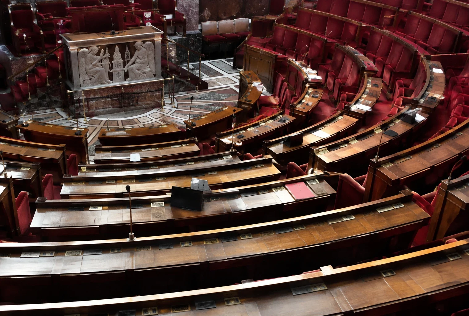Pupitres équipés de microphones et rangées de sièges dans un hémicycle parlementaire vide, sans élus ni documents visibles.