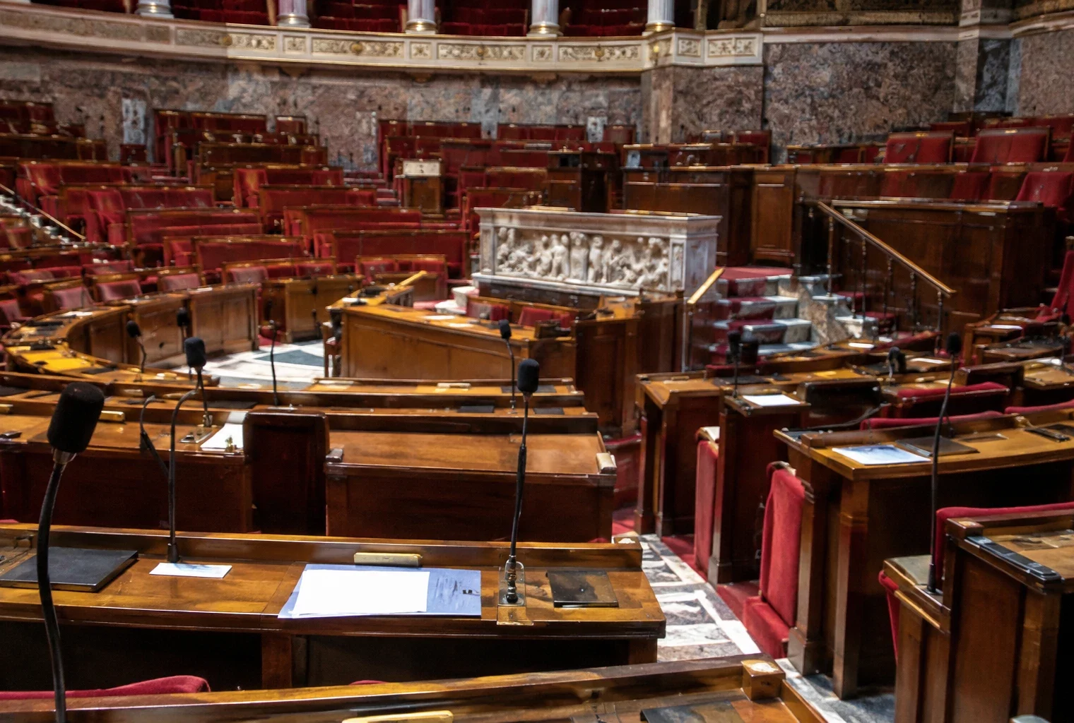 Pupitres munis de microphones disposés en rangées dans un hémicycle parlementaire aux sièges en gradins.