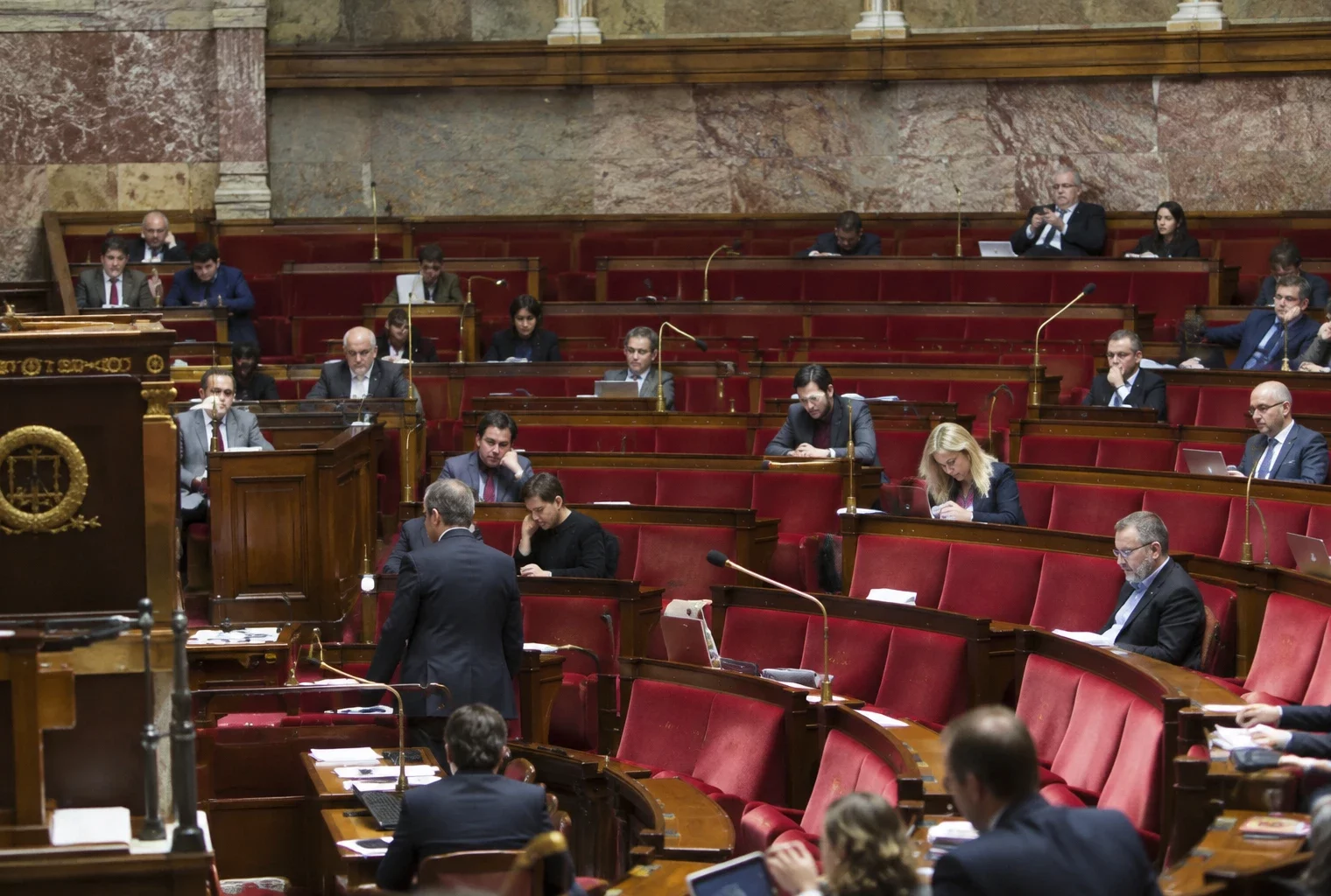 Pupitres équipés de microphones et sièges inoccupés dans un hémicycle parlementaire aux rangées concentriques.