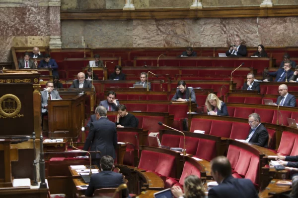 Pupitres équipés de microphones et sièges inoccupés dans un hémicycle parlementaire aux rangées concentriques.