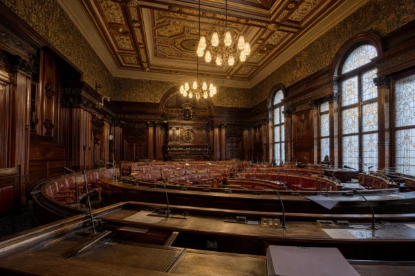 Hémicycle du Sénat vide au Palais du Luxembourg, pupitres de vote et boiseries sous des fenêtres en vitrail.