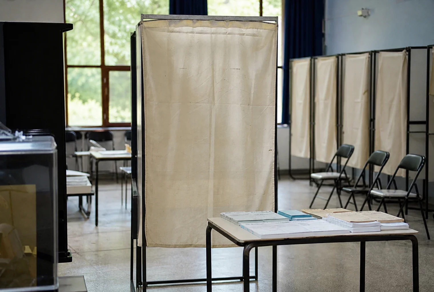 Un isoloir vide dans un bureau de vote, avec la table d’émargement et des chaises en arrière-plan.