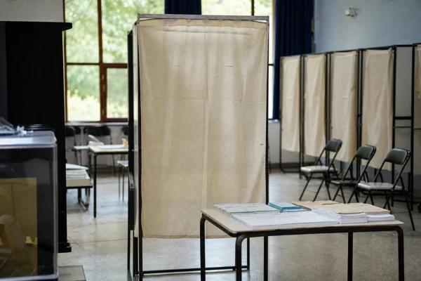 Un isoloir vide dans un bureau de vote, avec la table d’émargement et des chaises en arrière-plan.