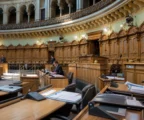 Hémicycle du Landtag de Saxe-Anhalt vu de loin, avec pupitres alignés, micros, estrade et panneaux sculptés.
