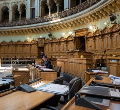 Hémicycle du Landtag de Saxe-Anhalt vu de loin, avec pupitres alignés, micros, estrade et panneaux sculptés.