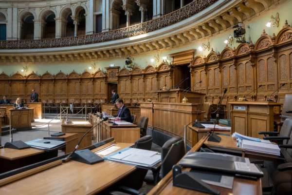 Hémicycle du Landtag de Saxe-Anhalt vu de loin, avec pupitres alignés, micros, estrade et panneaux sculptés.