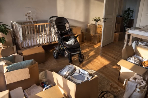 Cartons de déménagement et poussette réunis dans une pièce familiale où se trouvent aussi un petit lit et des affaires de bébé.