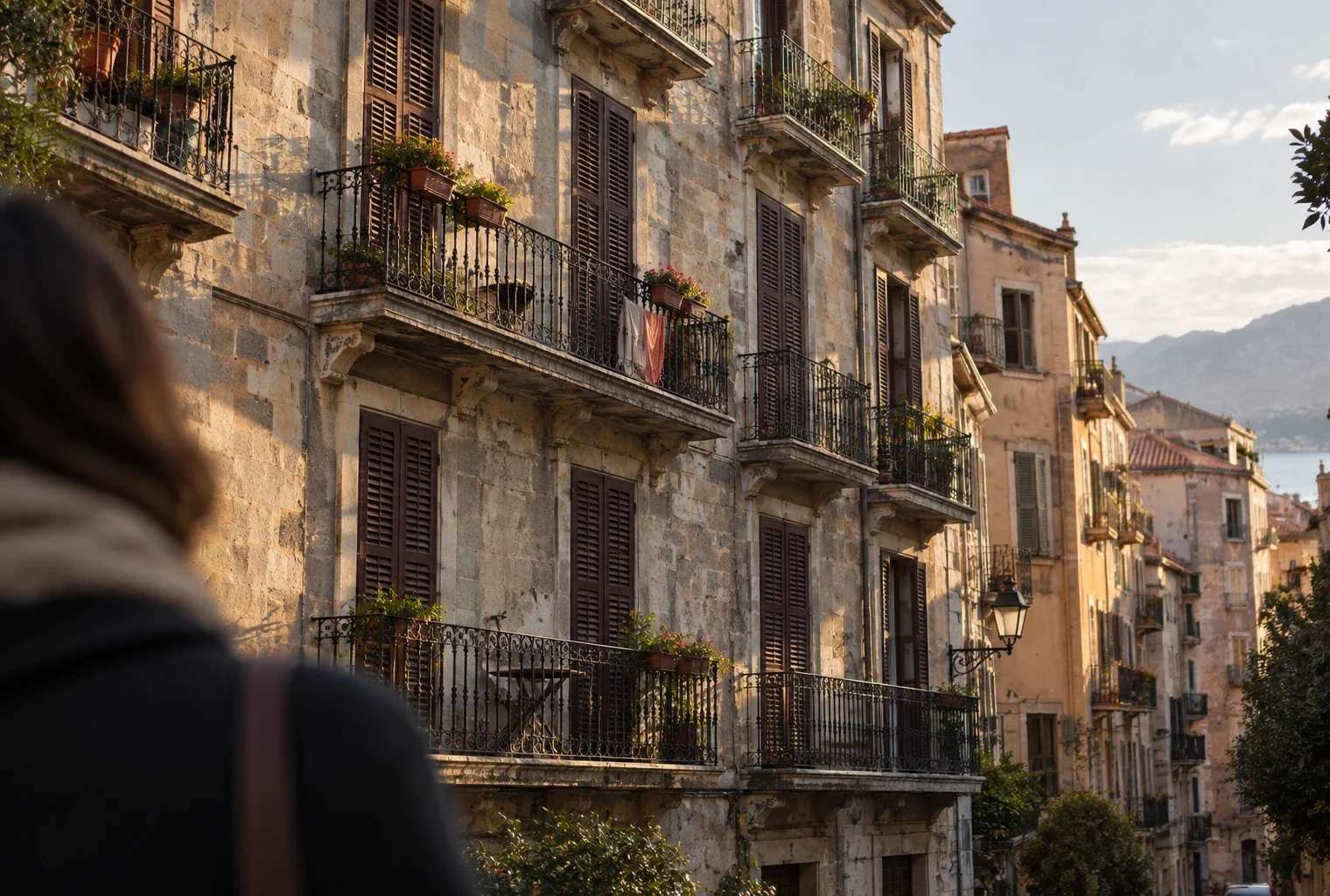 Façade d’un immeuble corse aux volets fermés et balcons patinés, dans une rue dense de logements résidentiels.