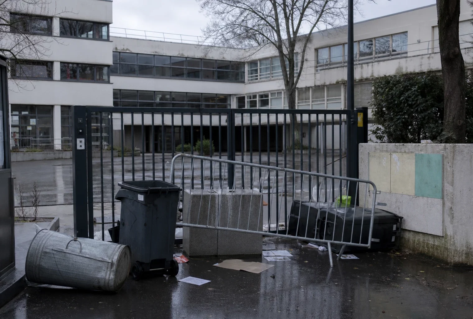 Entrée de lycée bloquée par des barrières, avec la cour vide derrière.
