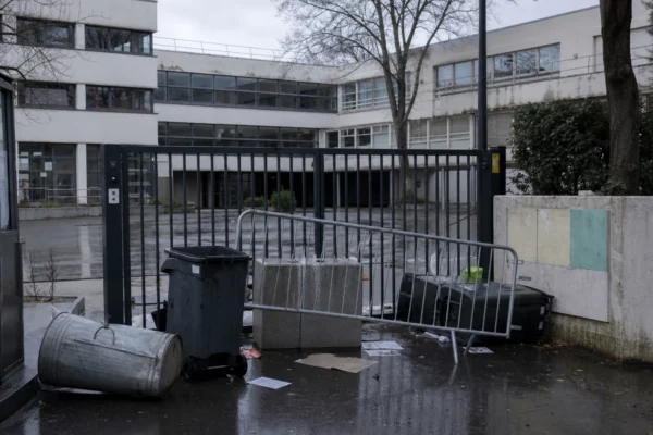 Entrée de lycée bloquée par des barrières, avec la cour vide derrière.