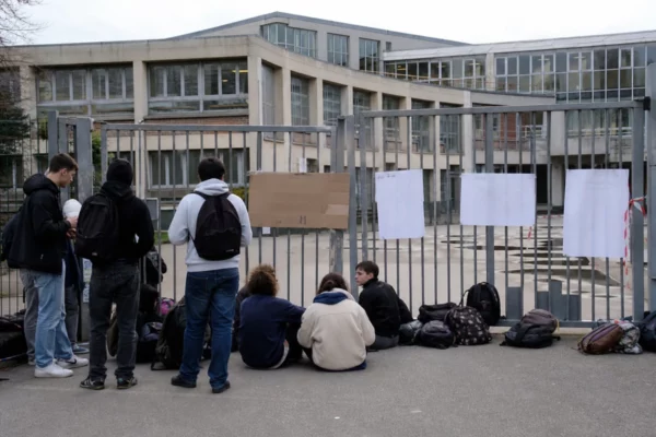 Des lycéens rassemblés devant l’entrée fermée d’un lycée bloqué, avec des sacs et des pancartes.