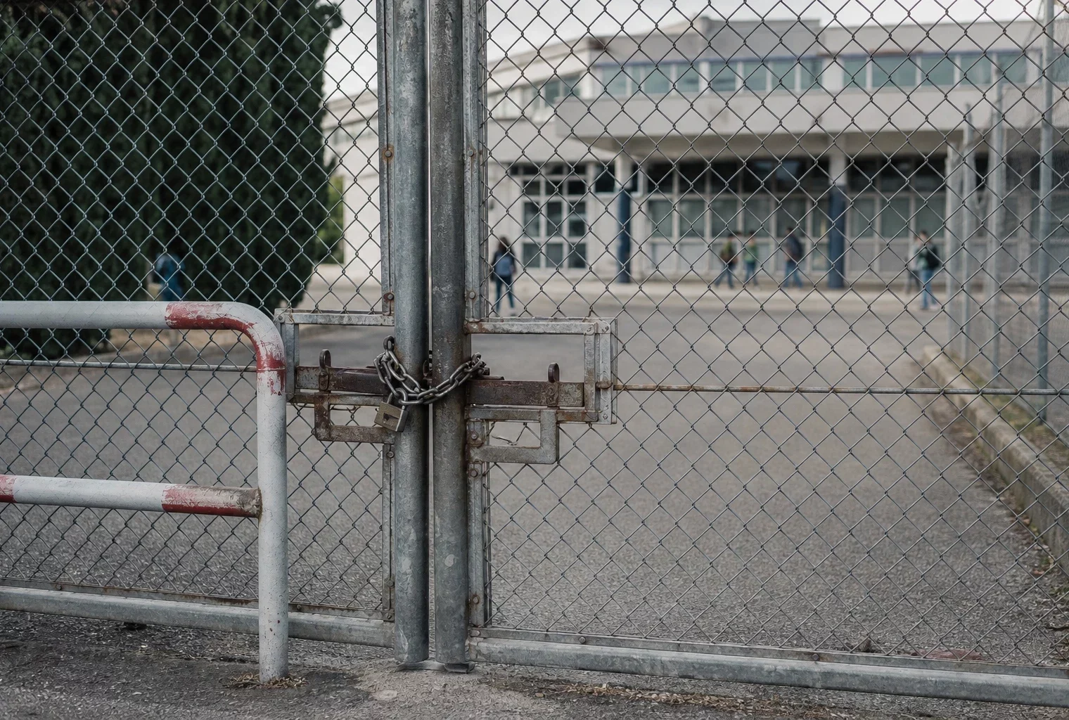 Grille de lycée fermée devant l’entrée, barrières et accès bloqué, façade scolaire floue en arrière-plan.