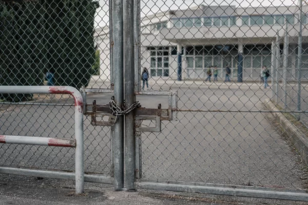Grille de lycée fermée devant l’entrée, barrières et accès bloqué, façade scolaire floue en arrière-plan.