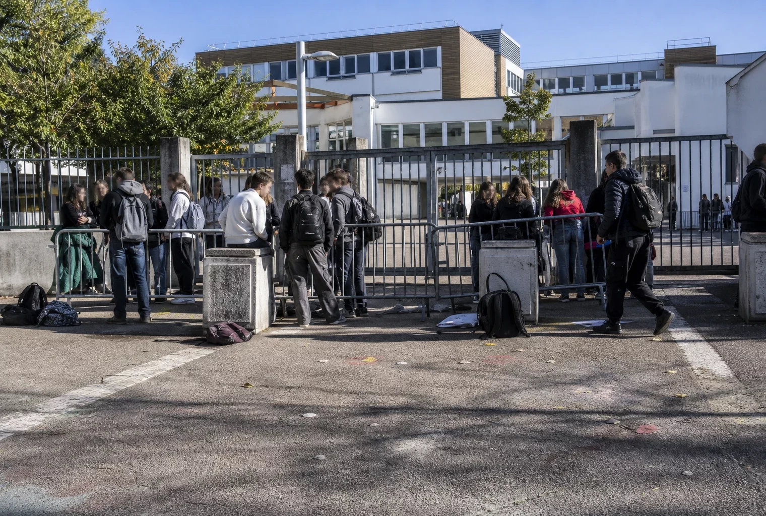 Entrée d’un lycée bloquée par des barrières et des élèves rassemblés devant le portail