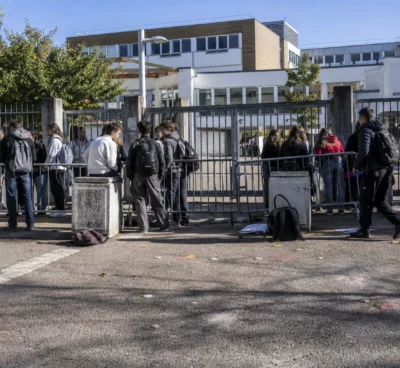 Entrée d’un lycée bloquée par des barrières et des élèves rassemblés devant le portail