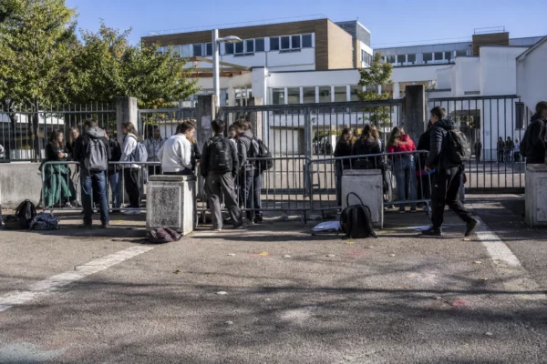 Entrée d’un lycée bloquée par des barrières et des élèves rassemblés devant le portail