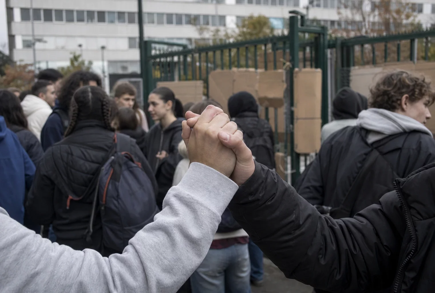 Des lycéens se rassemblent devant l’entrée d’un établissement bloqué, avec des pancartes et le portail en arrière-plan.