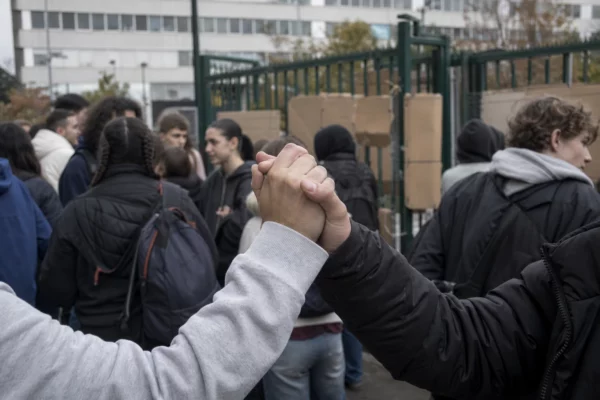 Des lycéens se rassemblent devant l’entrée d’un établissement bloqué, avec des pancartes et le portail en arrière-plan.