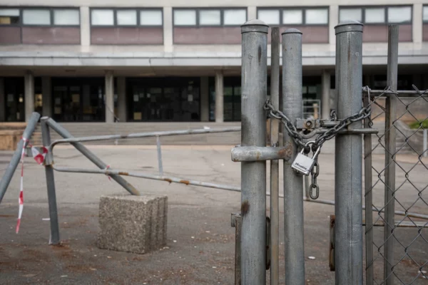 Grilles fermées d’un lycée public bloqué, chaînes et barrières improvisées devant un portail sobre, façade en arrière-plan.