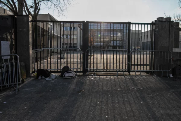 Grilles d’un lycée bloquées par des barrières, avec des sacs d’élèves posés au sol devant l’entrée.