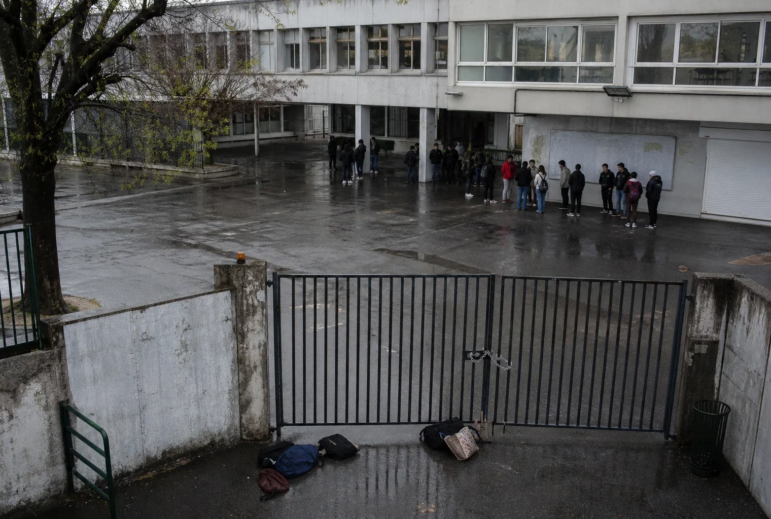 Entrée d’un lycée bloquée par des barrières, avec quelques sacs d’élèves au premier plan.