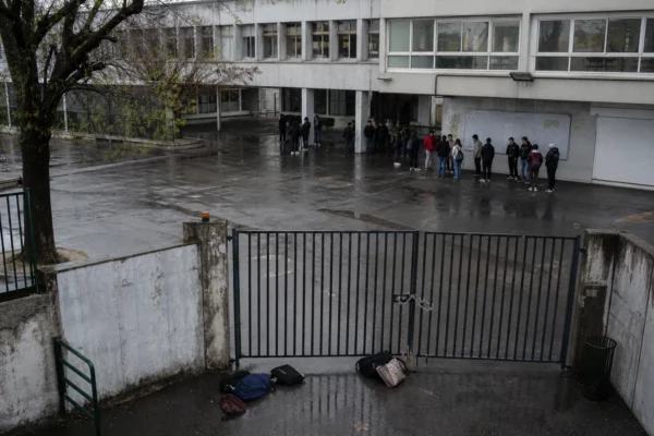 Entrée d’un lycée bloquée par des barrières, avec quelques sacs d’élèves au premier plan.