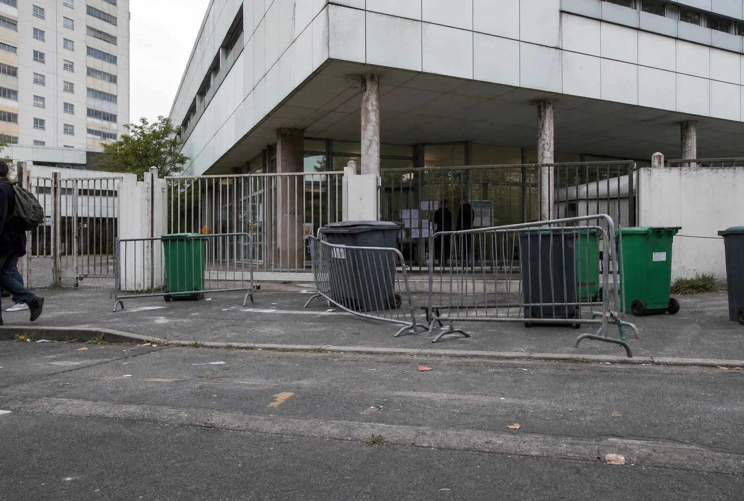 Entrée d’un lycée bloquée à Saint-Denis, avec barrières et poubelles devant les grilles.