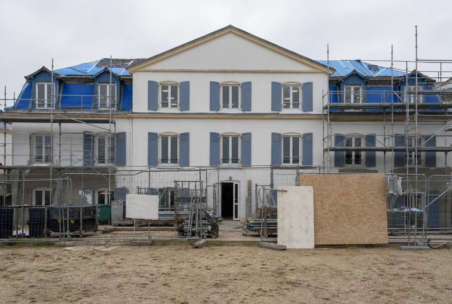 Façade d’un lycée public en travaux, avec échafaudages, barrières de chantier et cour d’établissement en arrière-plan.