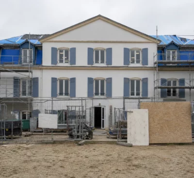 Façade d’un lycée public en travaux, avec échafaudages, barrières de chantier et cour d’établissement en arrière-plan.