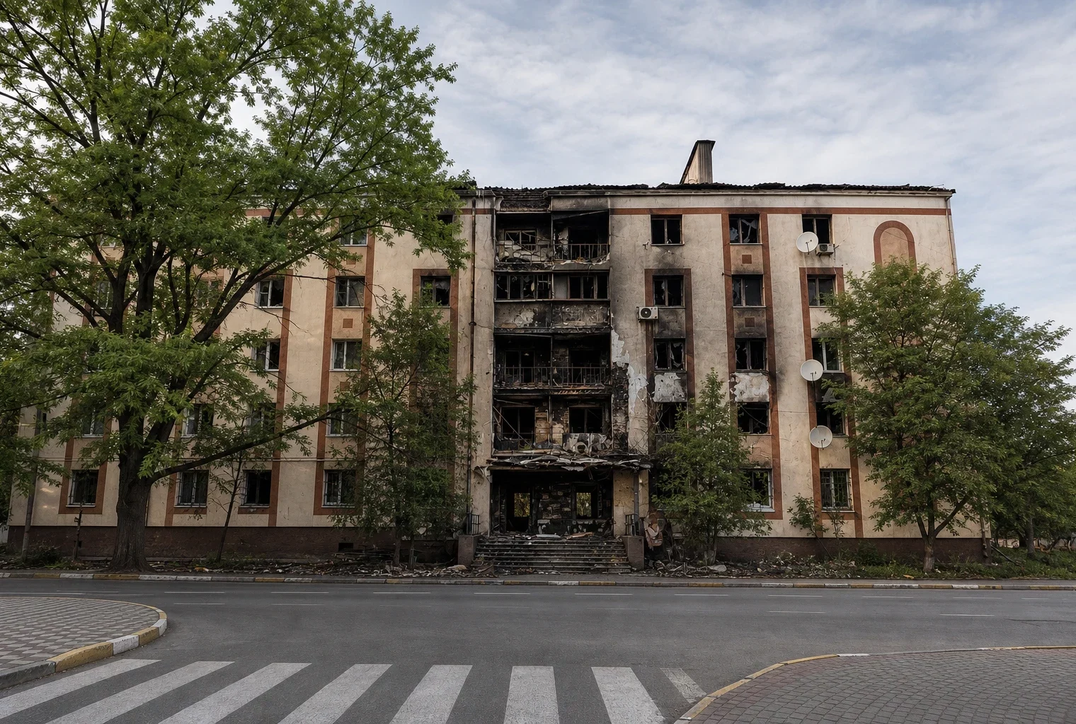 Façade de lycée incendiée en France, murs noircis, vitres brisées et débris devant un portail désert.