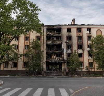 Façade de lycée incendiée en France, murs noircis, vitres brisées et débris devant un portail désert.