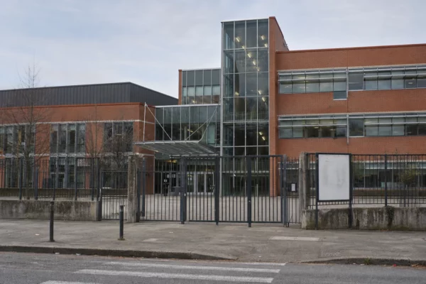 Entrée d’un lycée public français avec grilles, portail et façade en brique et verre, sous une lumière douce.