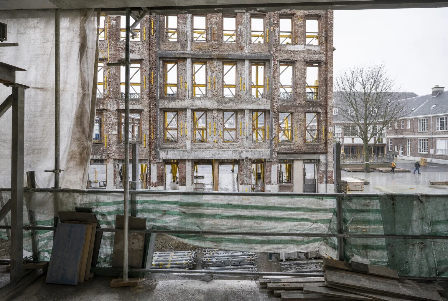 Façade de lycée public en rénovation, échafaudages et bâches de chantier dans une cour scolaire vide.