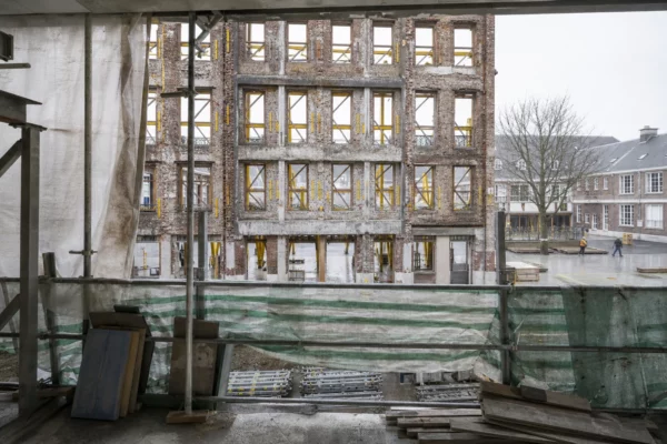Façade de lycée public en rénovation, échafaudages et bâches de chantier dans une cour scolaire vide.