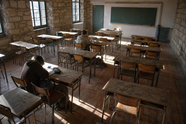 Salle de classe de lycée public français aux meubles usés, avec rangées de tables, tableau noir et murs marqués par le temps.