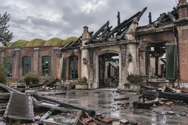 Façade d’un bâtiment municipal après un incendie, avec menuiseries noircies et débris sous un ciel gris pluvieux.