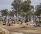 Hommages déposés sur un mémorial en plein air, au milieu d’un terrain ouvert, sans visiteurs visibles.