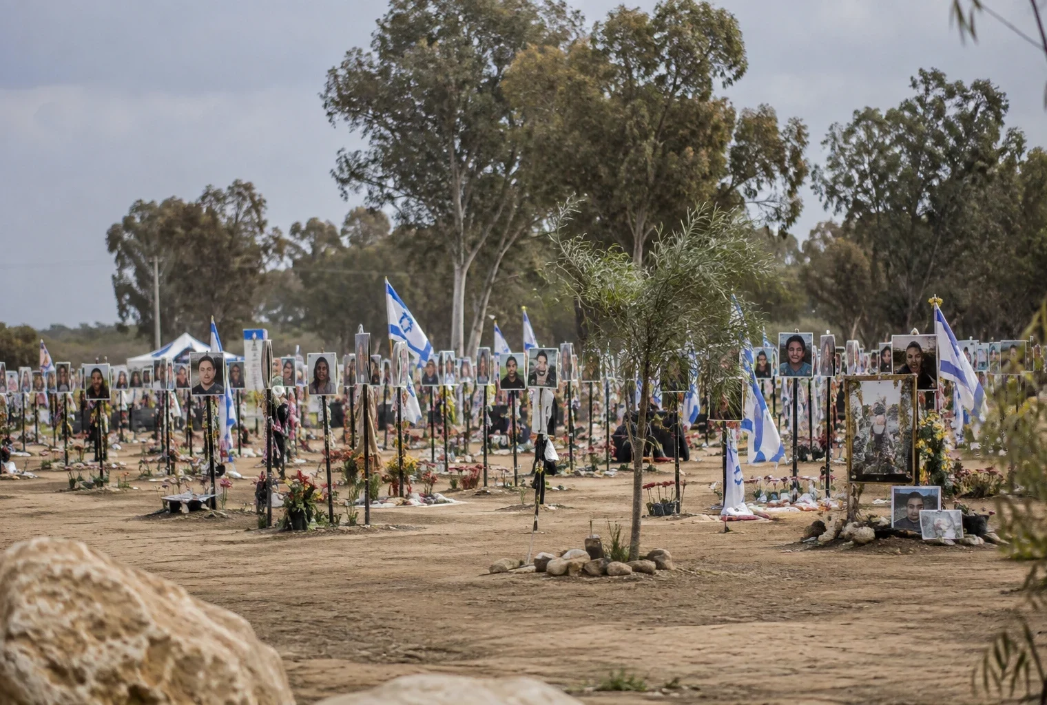 Hommages déposés sur un mémorial en plein air, au milieu d’un terrain ouvert, sans visiteurs visibles.