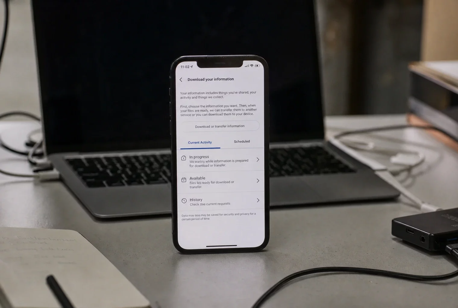 Un smartphone posé devant un ordinateur sur un bureau sobre, affichant des paramètres de téléchargement de données Messenger.
