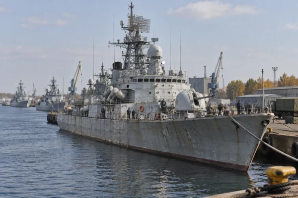 Un navire militaire soviétique gris amarré à un quai, avec des équipements portuaires et d’autres bateaux en arrière-plan.