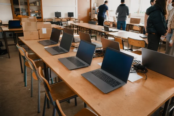 Distribution d’ordinateurs portables dans une salle de lycée, avec cartons et câbles sur des tables usées.