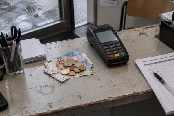 Pièces et billets en euros près d’un terminal de paiement sur un comptoir associatif, avec des formulaires vierges.