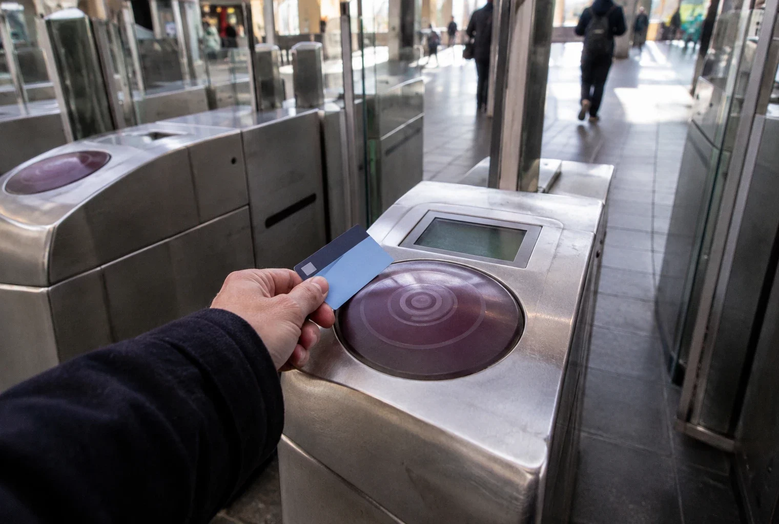 Une main approche une carte de transport d’un lecteur fixé à un portique, à l’entrée d’une station de train.