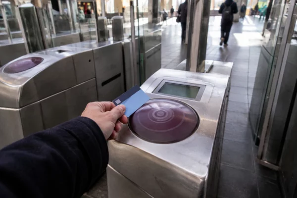 Une main approche une carte de transport d’un lecteur fixé à un portique, à l’entrée d’une station de train.